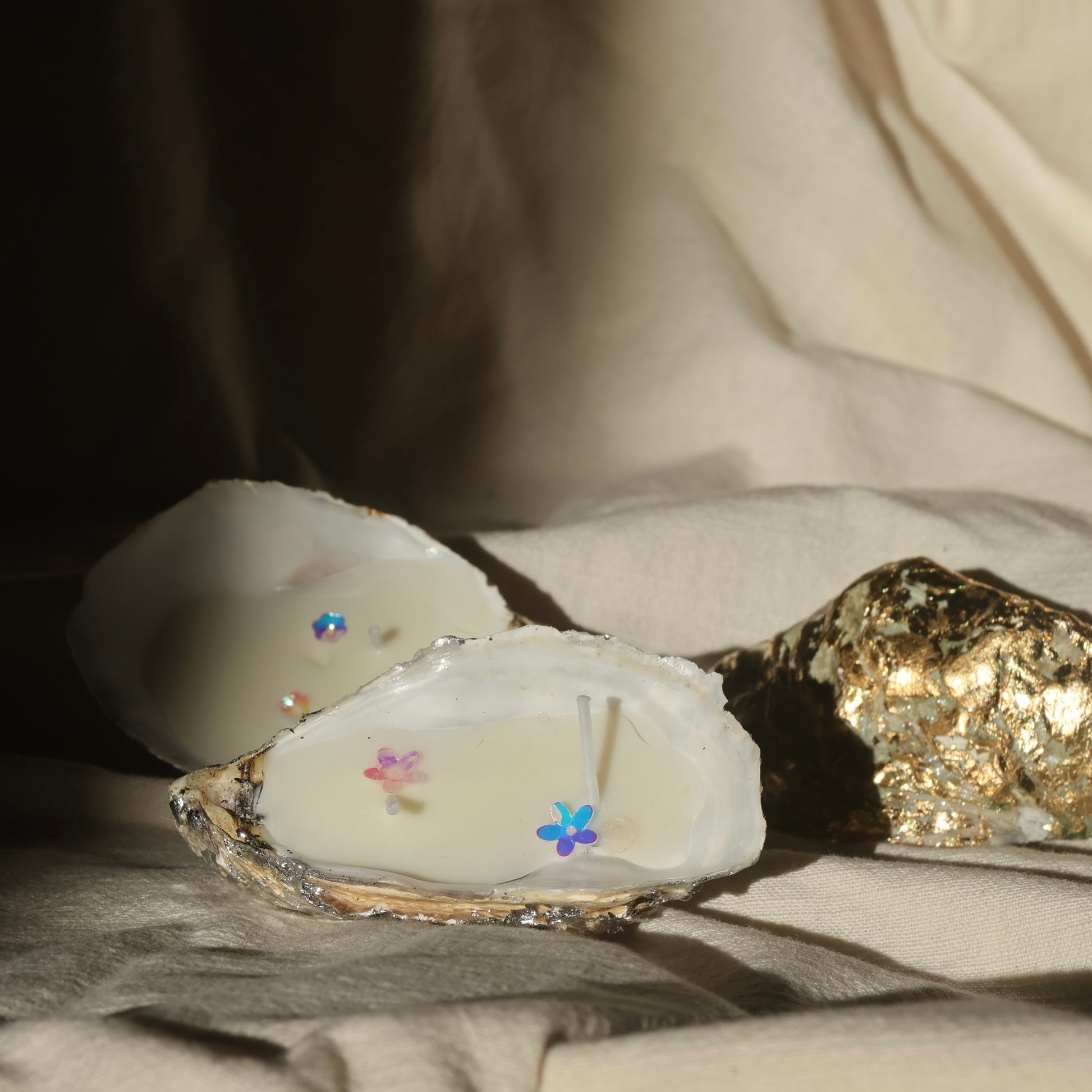 Glittery seashell candle by Lily Glow Home Decor with soft pastel flower accents on beige fabric 