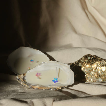 Glittery seashell candle by Lily Glow Home Decor with soft pastel flower accents on beige fabric 