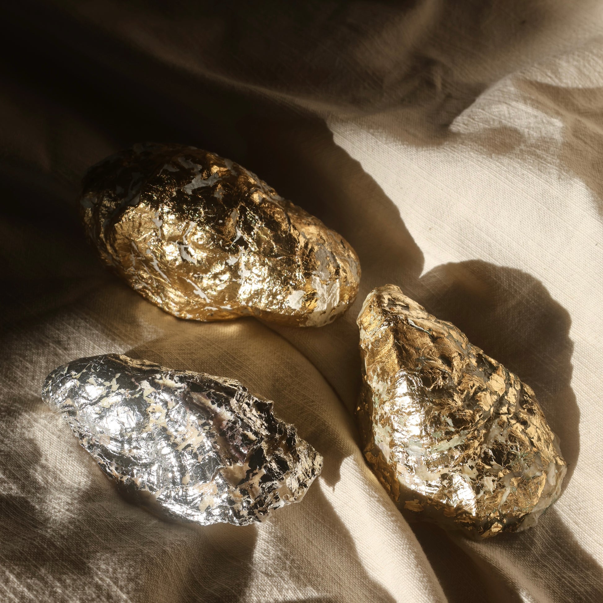 Set of golden and silver foil-wrapped seashell candles on neutral background by Lily Glow Home Decor
