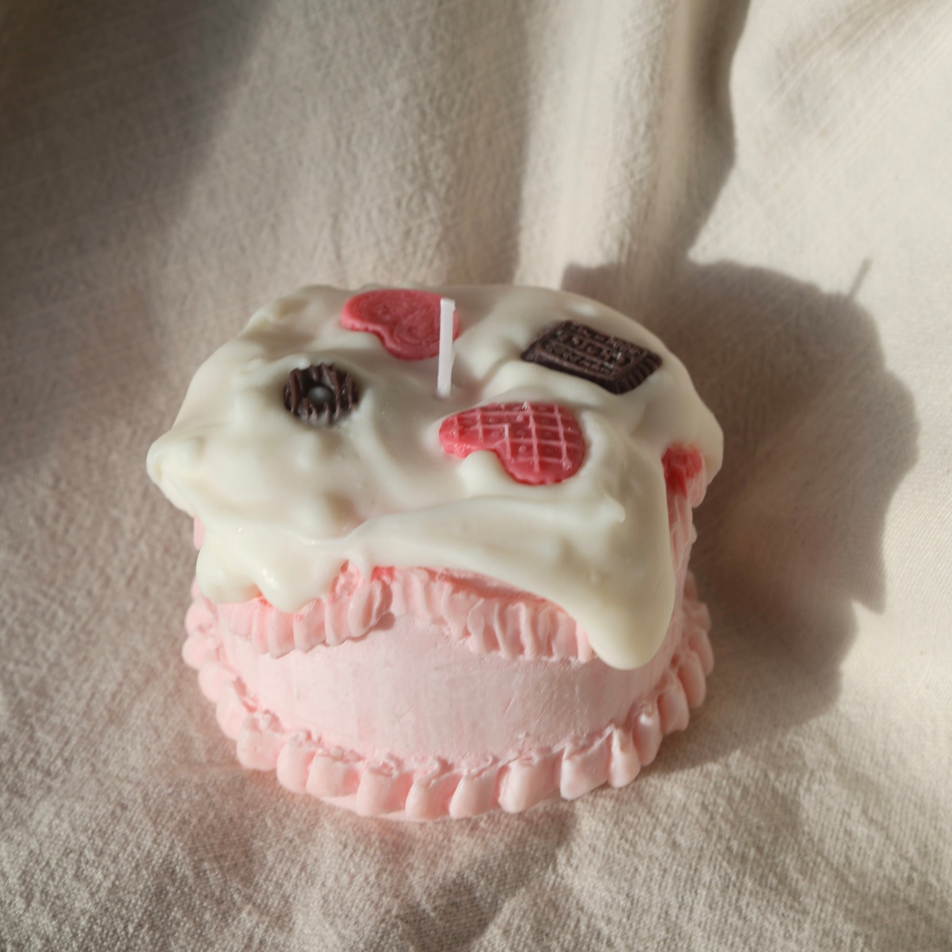 Pink cake-shaped candle with white frosting and decorative cookies by Lily Glow Home Decor