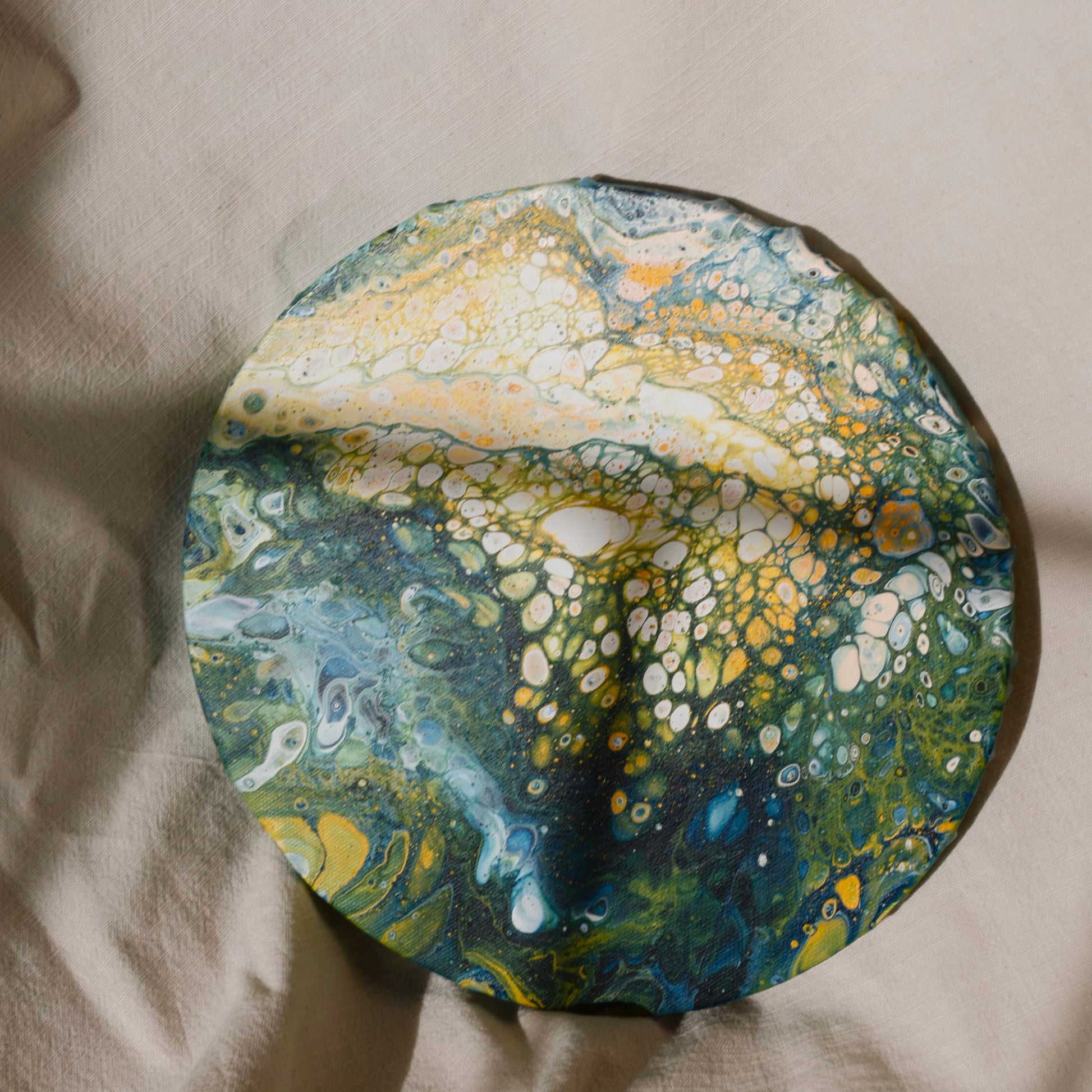 Close-up of a round canvas artwork with vibrant green and yellow abstract pattern on fabric background by Lily Glow Home Decor