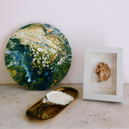 Round abstract painting in shades of green, yellow and white, placed on a marble surface next to home decor pieces by Lily Glow Home Decor